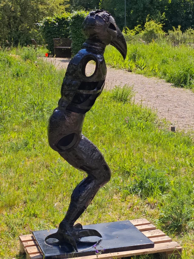 Hugo: die vollständige Stahlfigur mit Vogelkopf, offenem Rumpf und Füßen auf einer Standplatte.