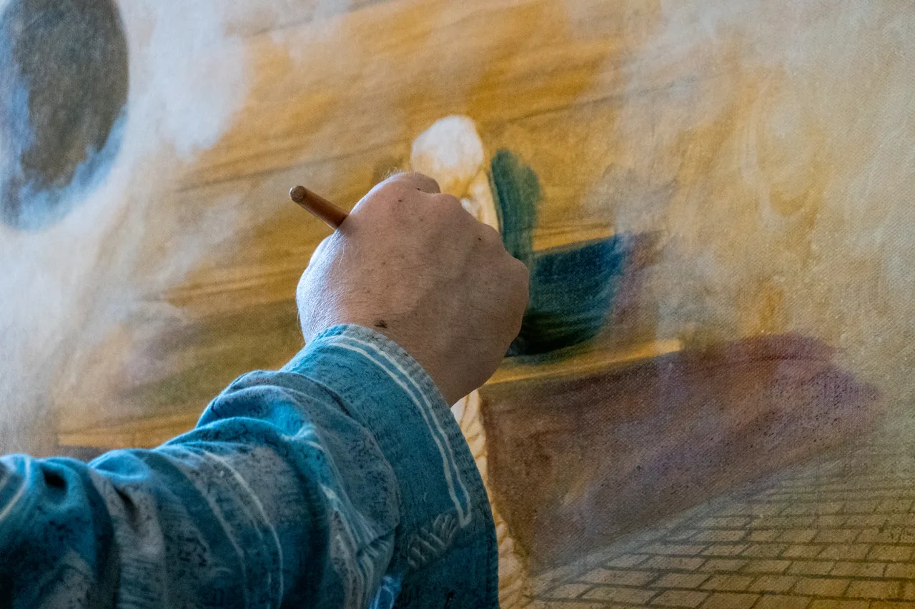 Eine Hand führt den Pinsel über die helle Figur auf der Leinwand.
