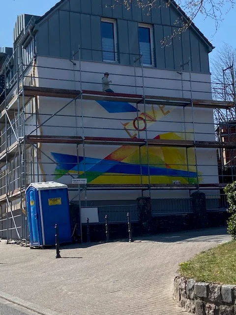 Arbeiten am Wandbild auf einem Gerüst vor der Fassade.