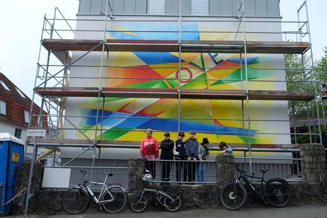 Gruppenaufnahme vor dem Gerüst der bemalten Fassade.