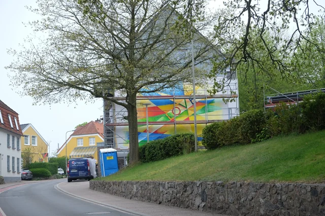 LOVE-Wandbild mit Gerüst, Baum und Hecke im Straßenraum.