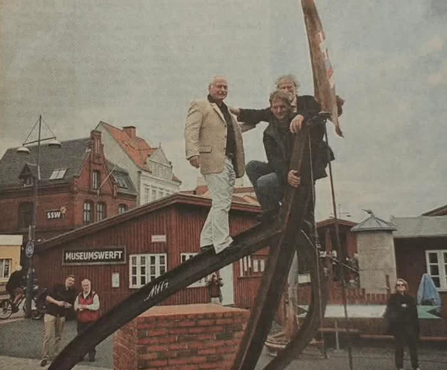 Drei Künstler auf der bootsförmigen Skulptur im Flensburger Hafen, überliefertes Pressefoto