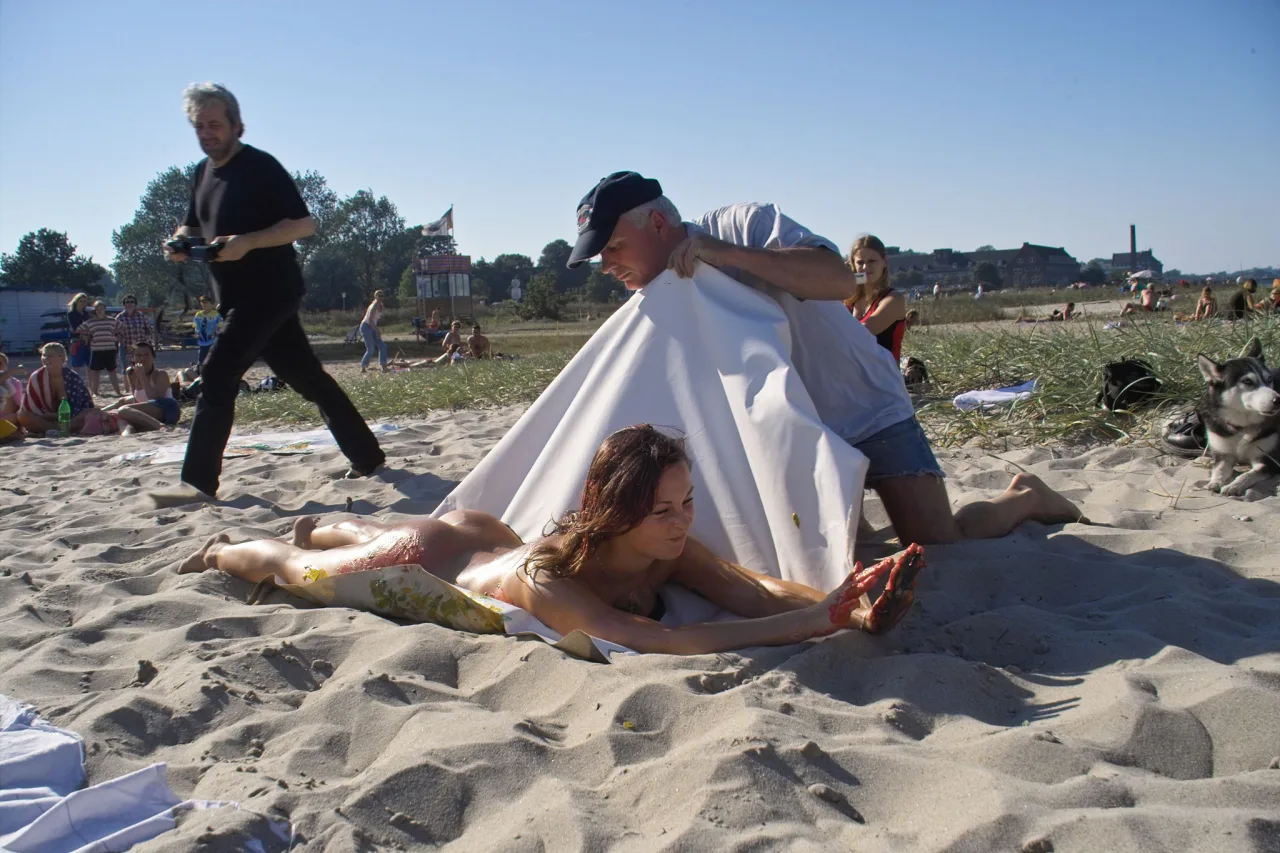 Kowalke breitet eine weiße Leinwand aus, ein Modell liegt daneben im Sand.