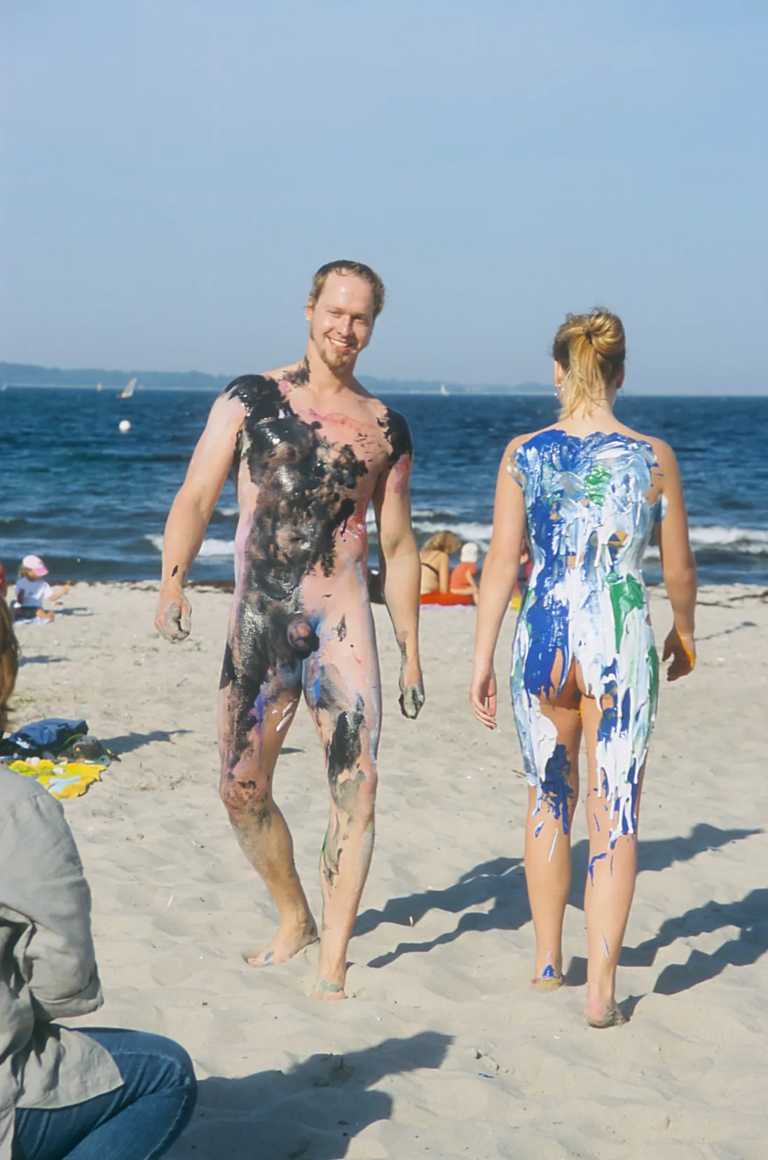 Zwei bemalte Modelle gehen über den Strand in Richtung Wasser.